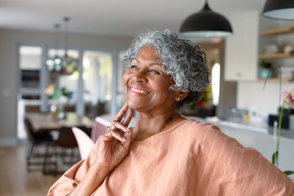 An older woman with gray hair smiles confidently at home, representing good diabetes management and healthy aging.
