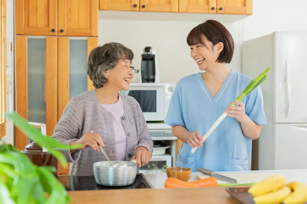 Caregiver cooking with an older adult in the kitchen, supporting healthy aging at home through nutrition and companionship.