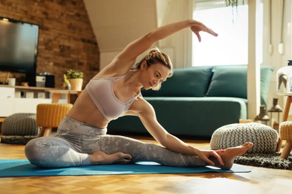 Woman stretching on a yoga mat at home, practicing grounding exercises for stress relief.