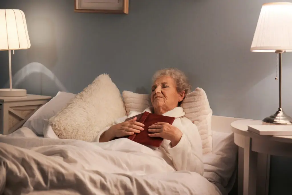 Older adult resting in bed after reading, a healthy sleep habit that supports aging well at home.